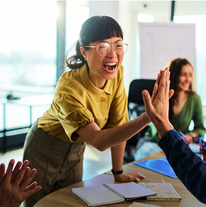 Two people at a conference table giving each other a high-five, showing the collaborative nature of social media strategy.